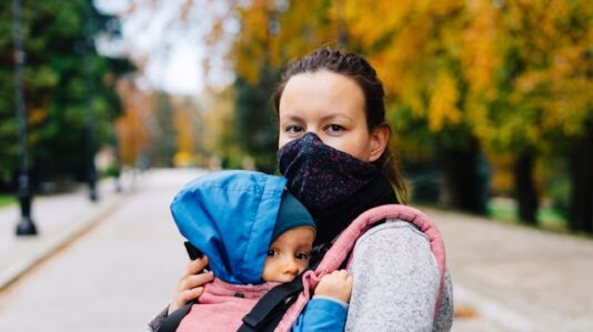 a mother wearing face mask carrying her baby