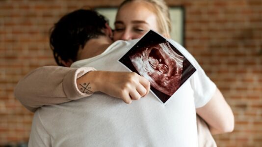 a woman holding an ultrasound embraced by her man