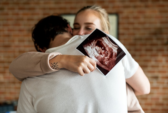 a woman holding an ultrasound embraced by her man